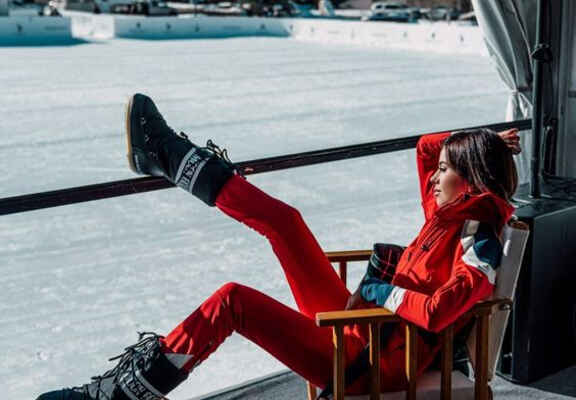 femeie in costum de schi rosu cu cizme Moon Boot negre